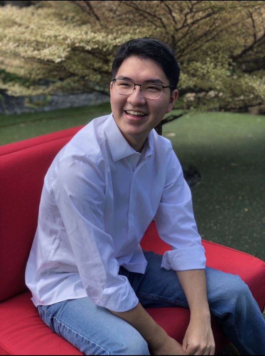 Keisen Kim smiling, seated on a red sofa outdoors